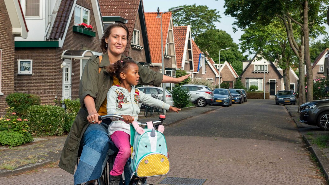 Een moeder fietst met haar dochter voor op de fiets in een zonnige en groene straat.