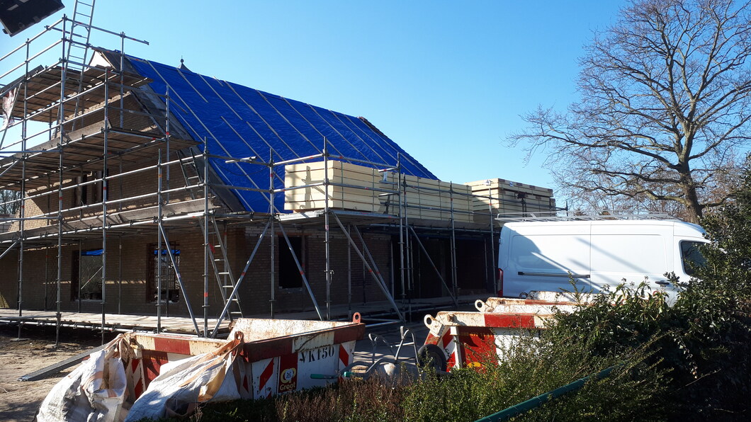 foto van een huis dat verbouwd wordt, met isolatiemateriaal op de steigers naast het dak.