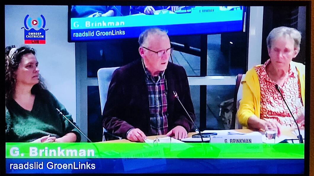 Foto van een beeldscherm waarop de raadsvergadering te zien is. In het midden van de foto zit GroenLinks fractievoorzitter Gerard Brinkman.