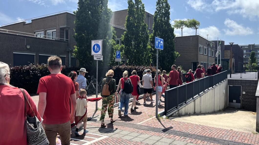 Foto van 1 van de 2 rode lijn demonstraties in Castricum. Mensen in rode kleding vormen een lijn voor het gemeentehuis. 