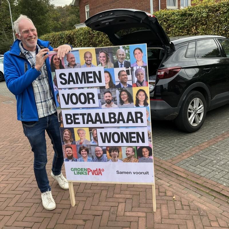 Foto van vrijwilliger Hans Min naast een van de verkiezingsborden.