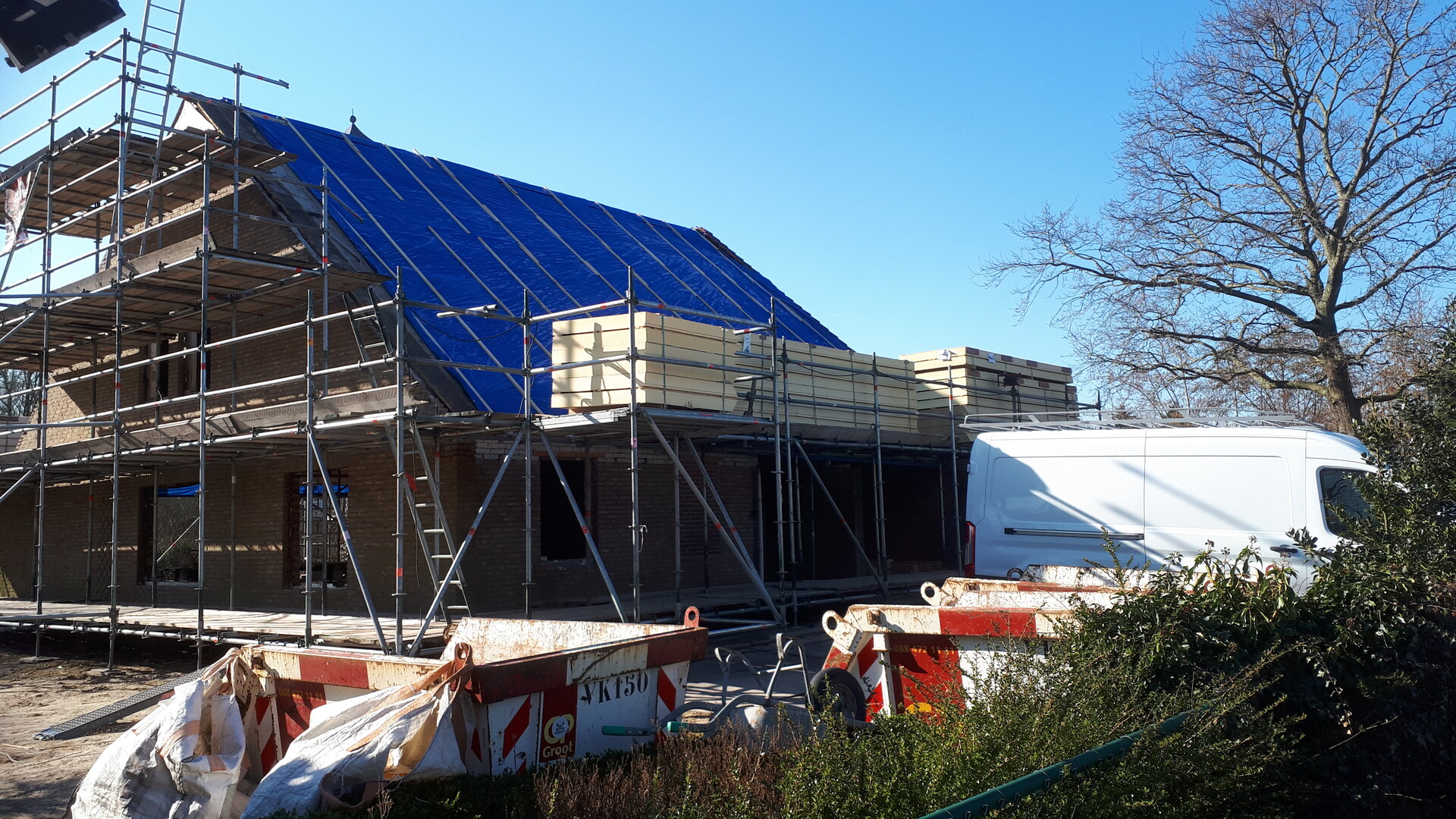 foto van een huis dat verbouwd wordt, met isolatiemateriaal op de steigers naast het dak.