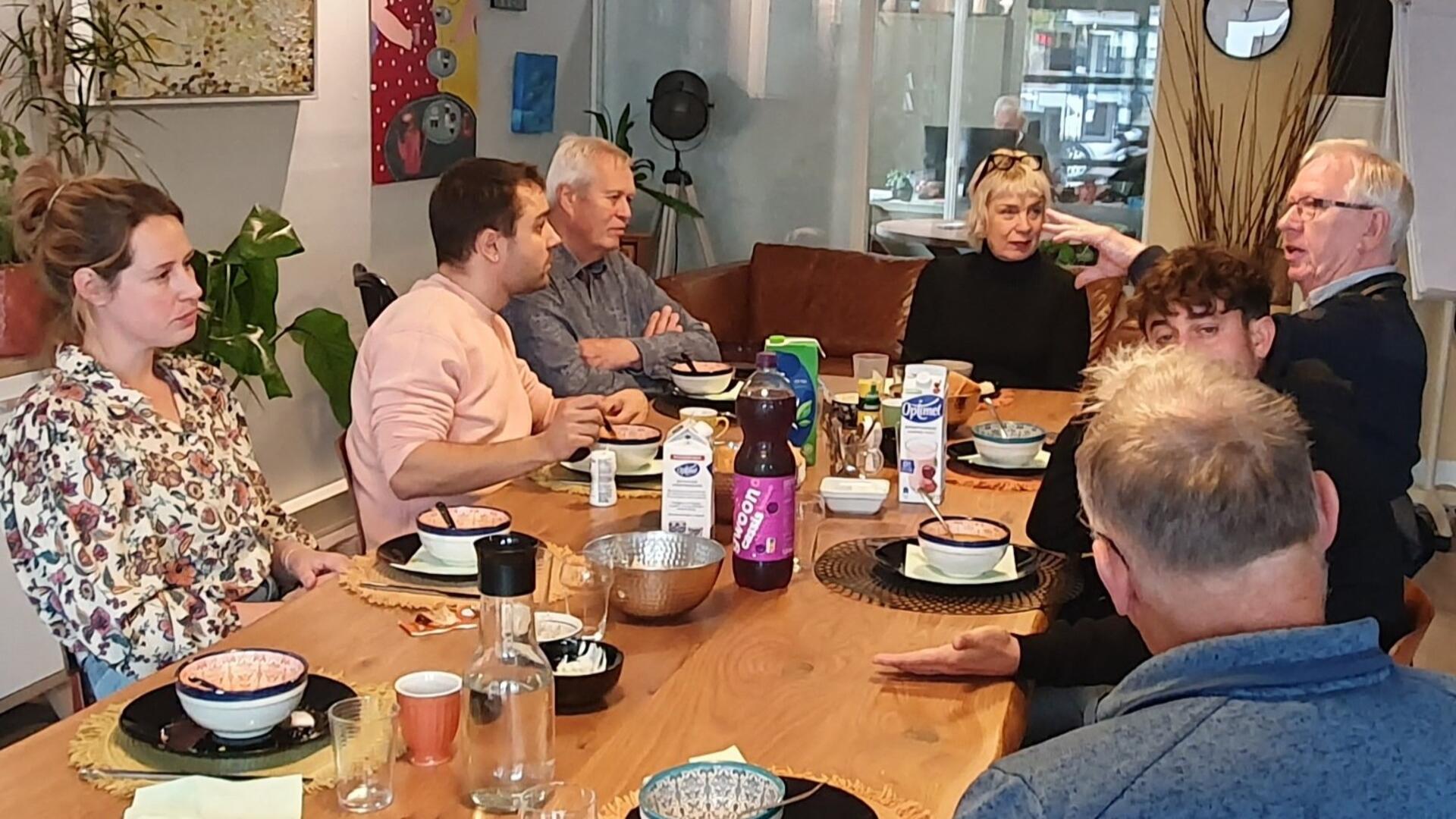 Kandidaat-kamerlid is in gesprek met jongerenwerkers en raadsleden bij Stichting Welzijn. Ze zitten om een tafel gedekt voor de lunch.